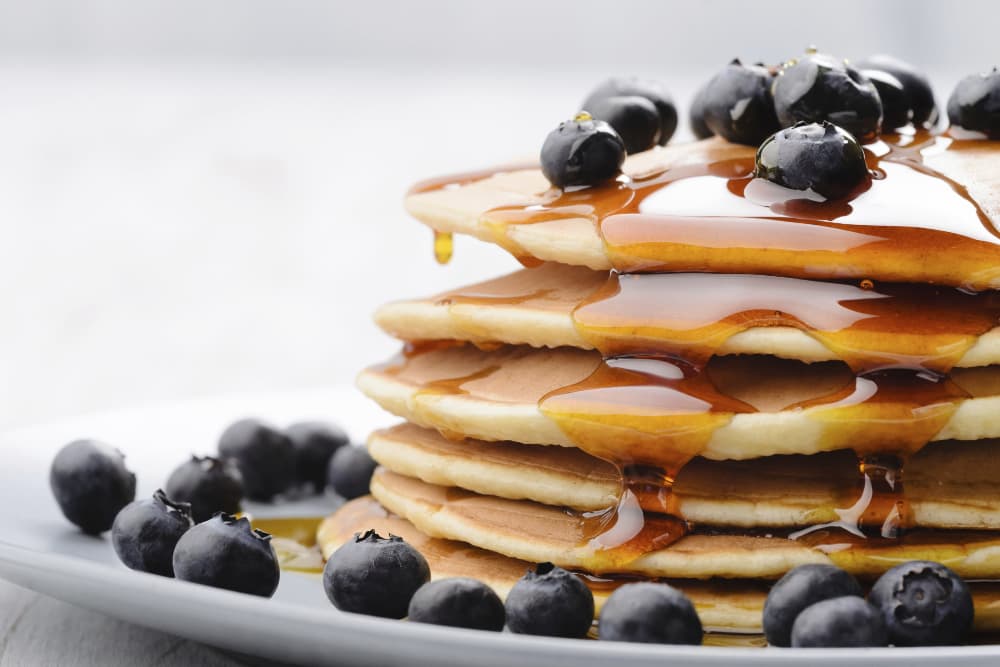 A stack of pancakes with fresh blueberries and maple syrup dripping down the sides from the top.
