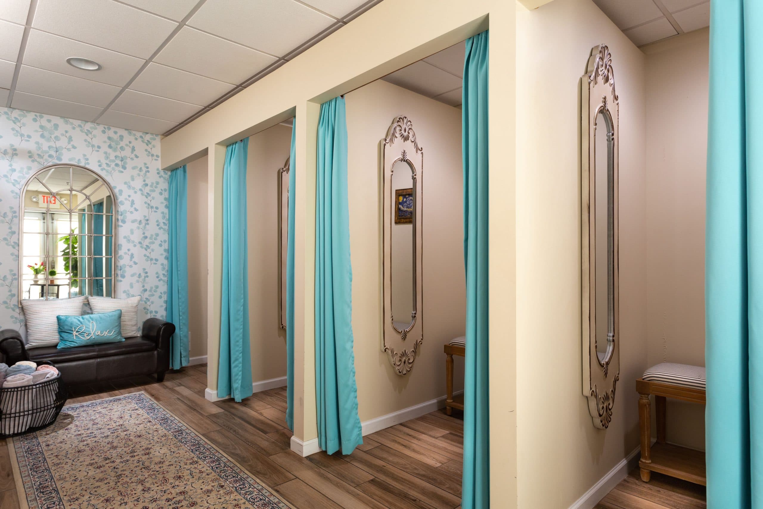 An elegant dressing room area in a spa. There are several individual dressing rooms with blue curtains and mirrors. A plush leather sofa and a patterned rug are located in the hallway.