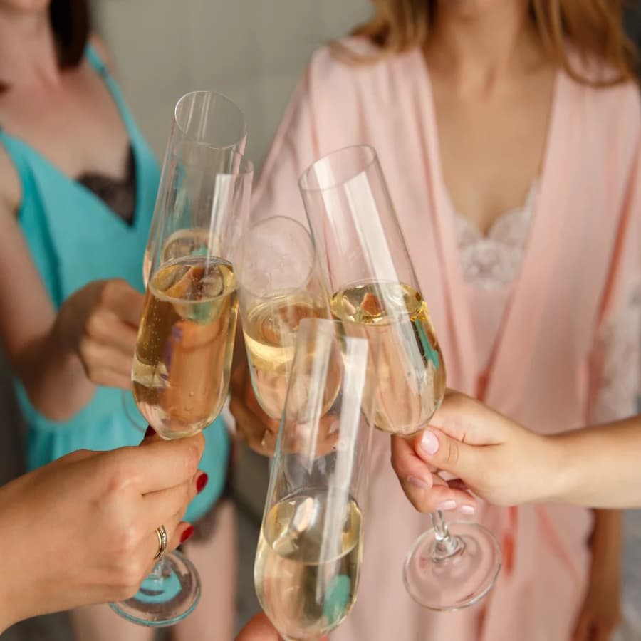 Several women gathered around in a circle in satin bathrobes toasting with glasses of champagne.