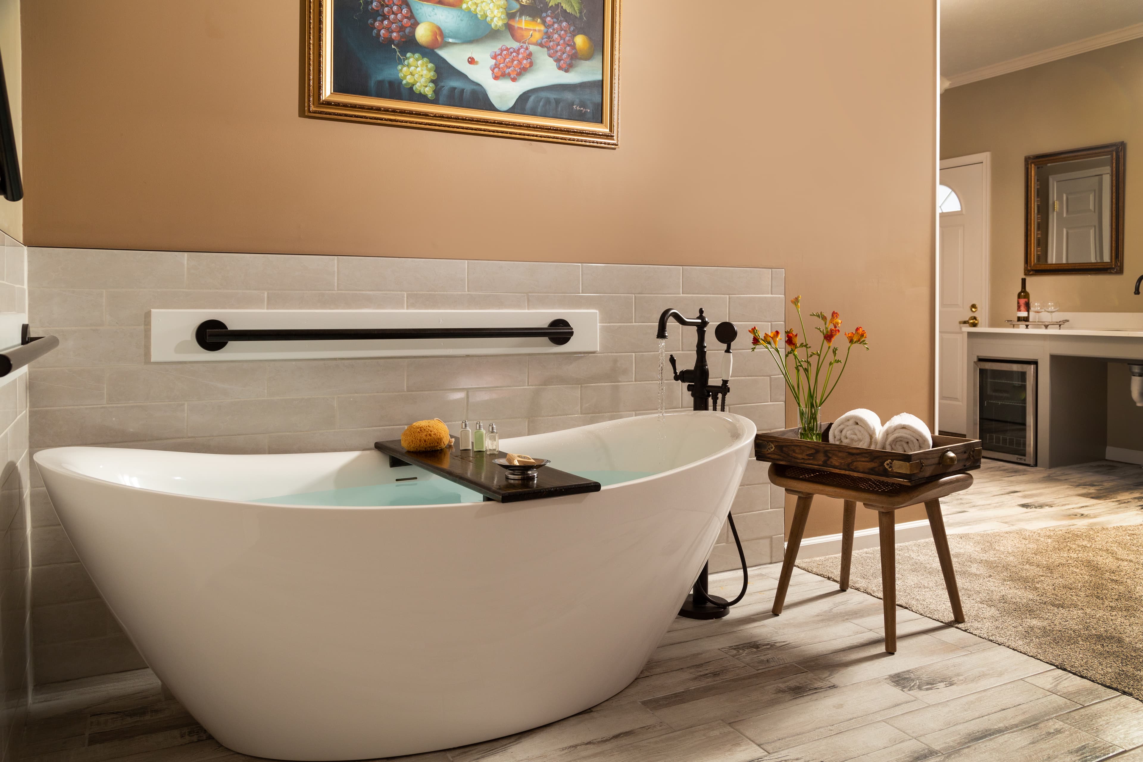 A modern bathroom featuring a freestanding white tub, a wooden tray with spa items, and a flower arrangement.