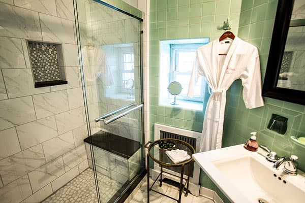 A modern bathroom featuring a glass shower, marble tiles, a plush bathrobe, and a small vanity with toiletries.
