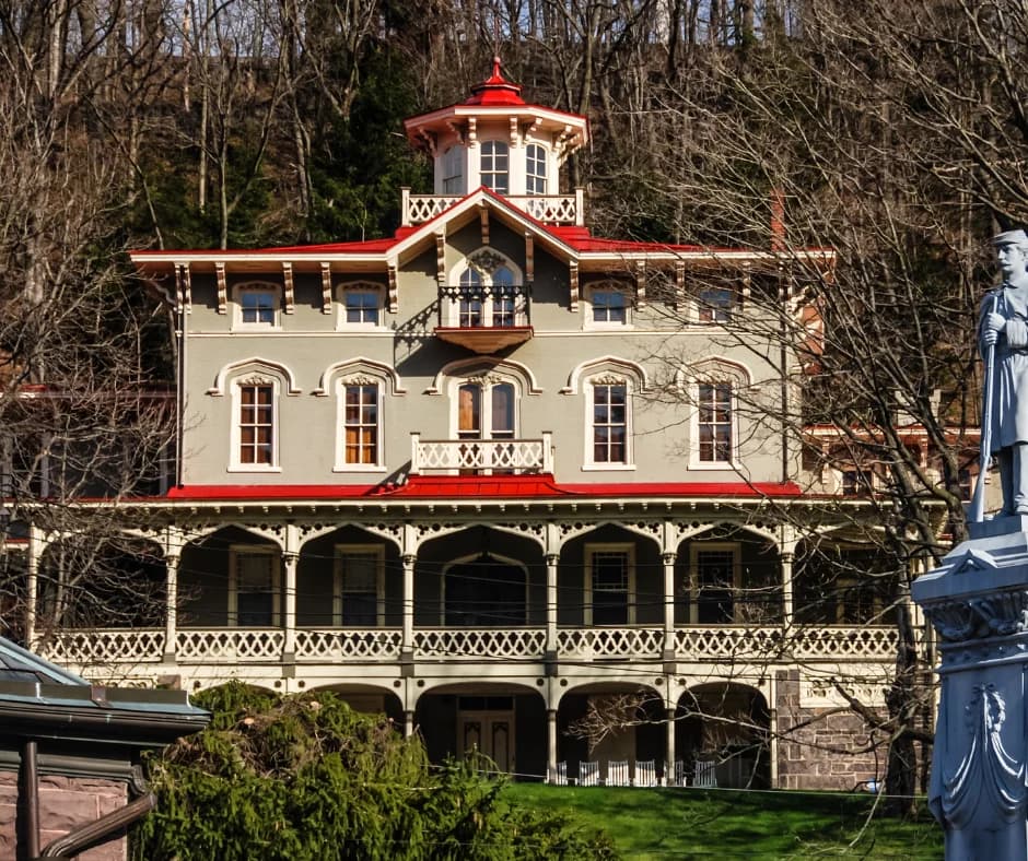 A Victorian-style house with a red roof and balcony, surrounded by trees.