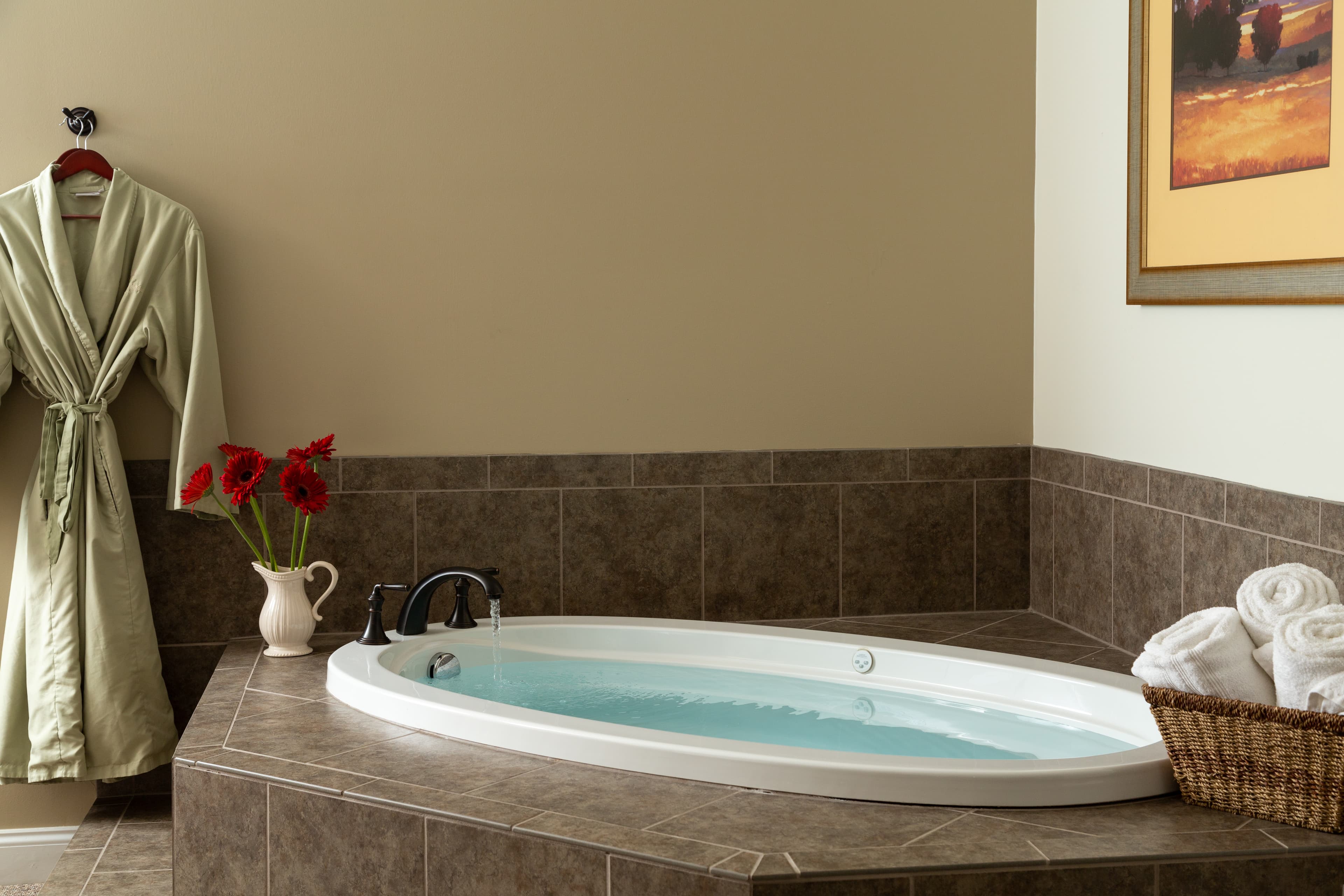 A spacious bathroom featuring a white oval bathtub, plush towels, a green robe, and decorative flowers.