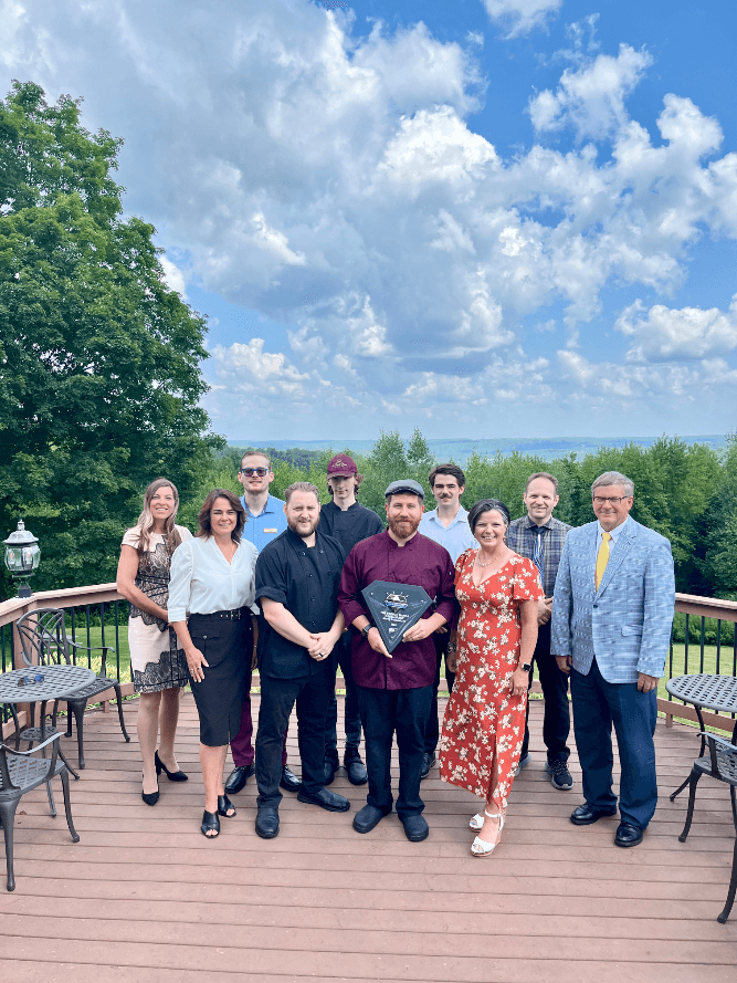 A group of people standing on a wood deck in front of trees and mountains receiving the AAA Restaurant Award for 2024.