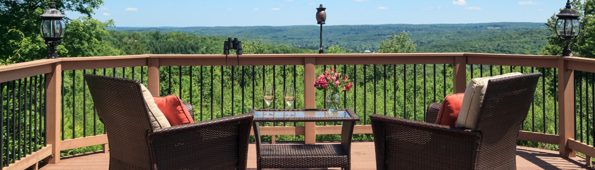 A deck with two chairs, a table, and a glass vase with flowers, overlooking the Pocono mountains.