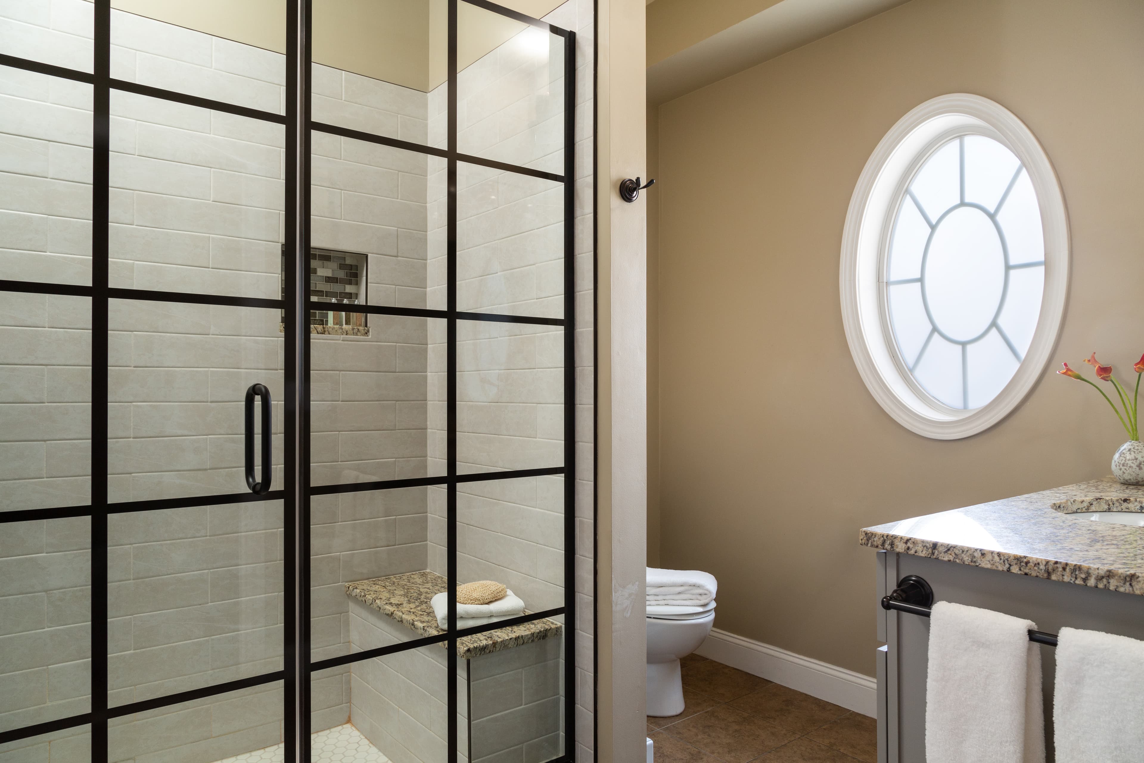 Modern bathroom featuring a glass shower, granite countertop, and an oval window.