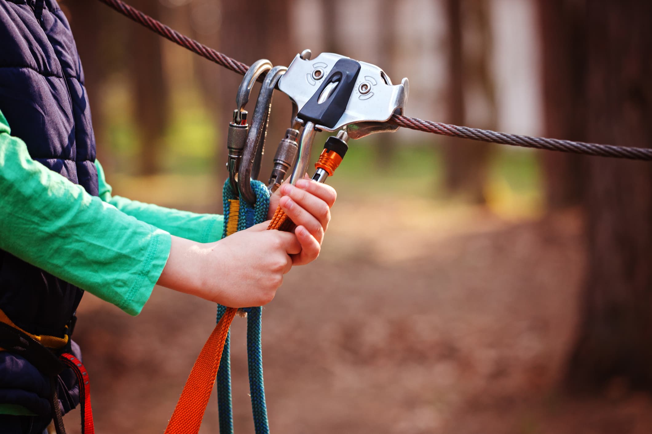 A person in a green shirt grips climbing gear attached to a cable in a forest setting. A person in a green shirt grips climbing gear attached to a cable in a forest setting.