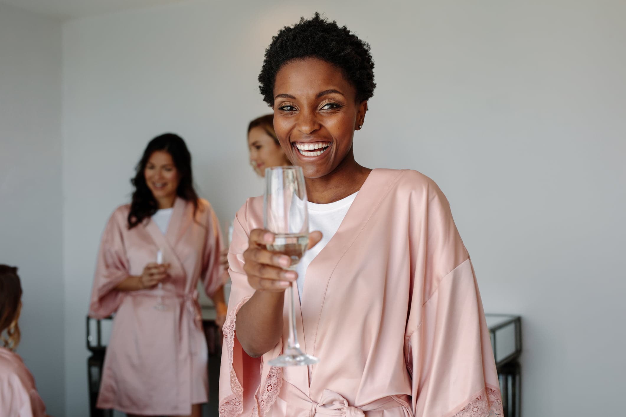 A smiling woman in a pink robe holds a champagne glass while celebrating with friends. A smiling woman in a pink robe holds a champagne glass while celebrating with friends.