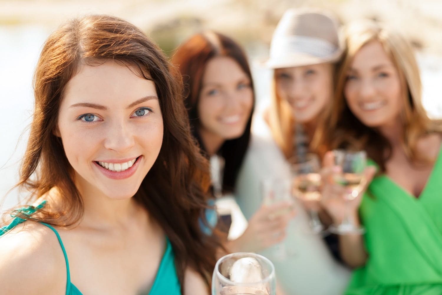 A group of four women smiling and enjoying drinks outdoors by the water.
