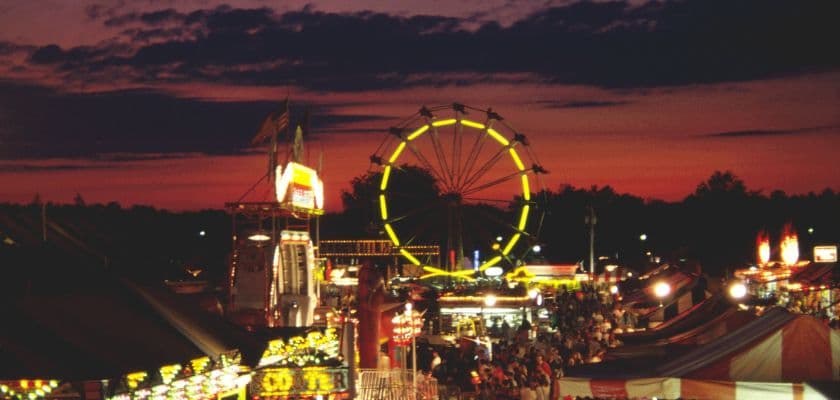 A vibrant fairground scene at sunset with a Ferris wheel and lively crowds.