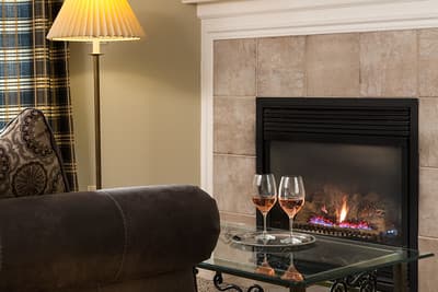 A cozy living room scene featuring a sofa, a glass coffee table with two glasses of rosé, and a gas fireplace.