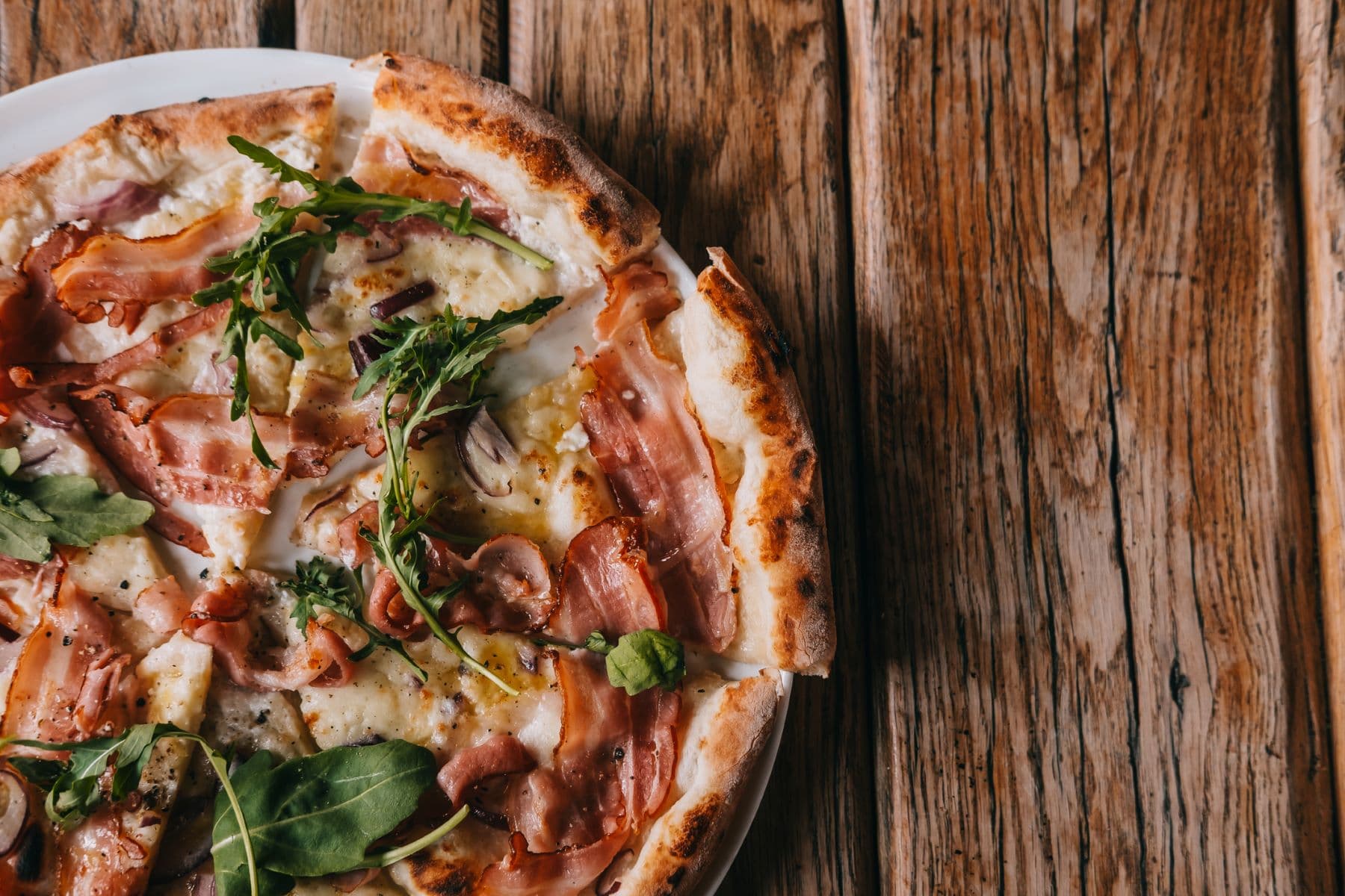 A freshly baked pizza topped with ham, greens, and cheese on a wooden table.