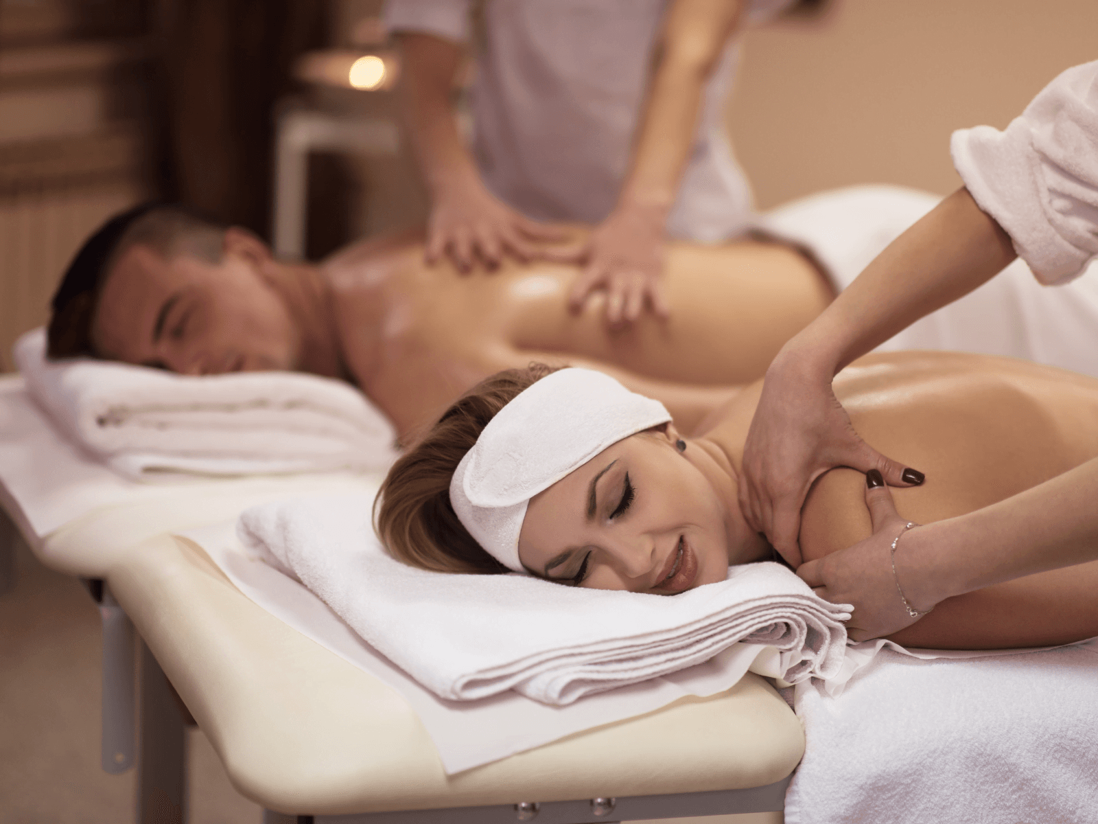A woman and a man receive relaxing massages on adjacent tables in a serene spa setting. A woman and a man receive relaxing massages on adjacent tables in a serene spa setting.