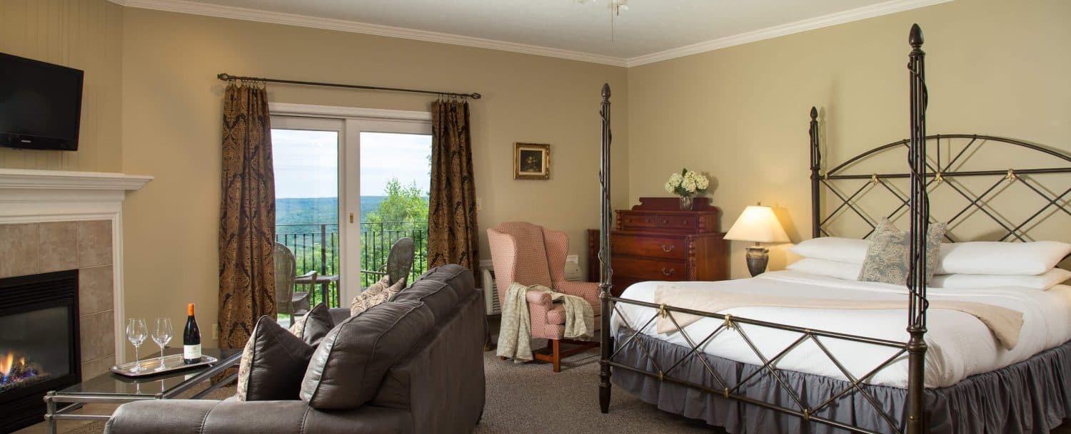 A cozy bedroom featuring a four-poster bed, a sitting area, and a scenic view through large windows.