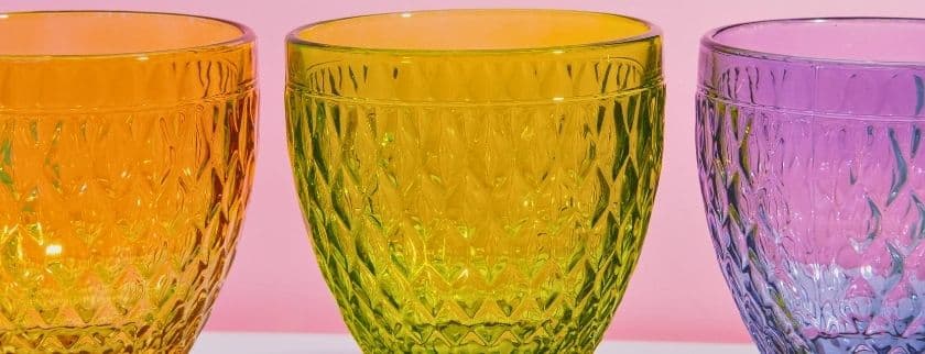 Three textured glass bowls in orange, green, and purple against a pink background.