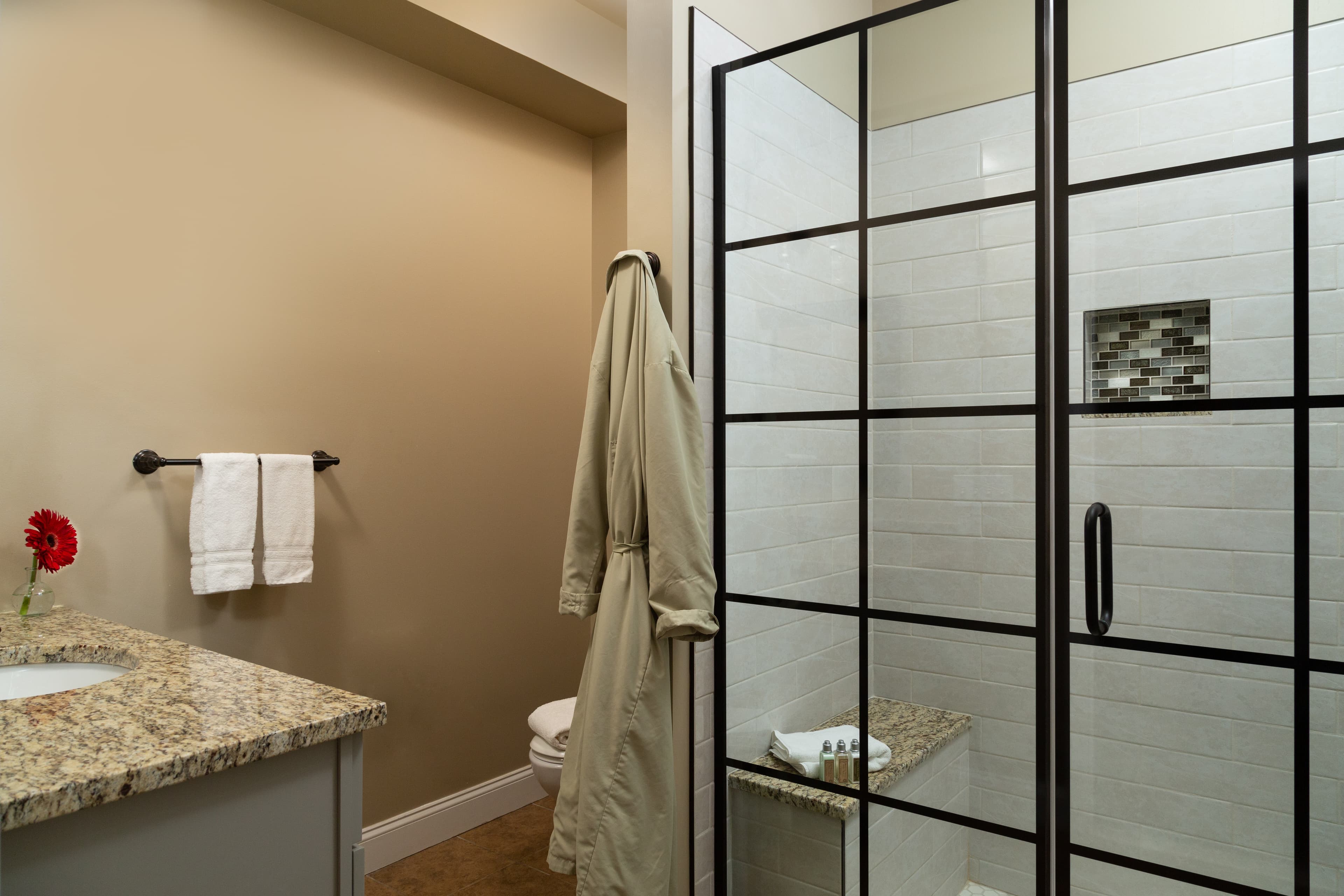 A modern bathroom featuring a glass shower, granite countertop, and a bathrobe hanging nearby.
