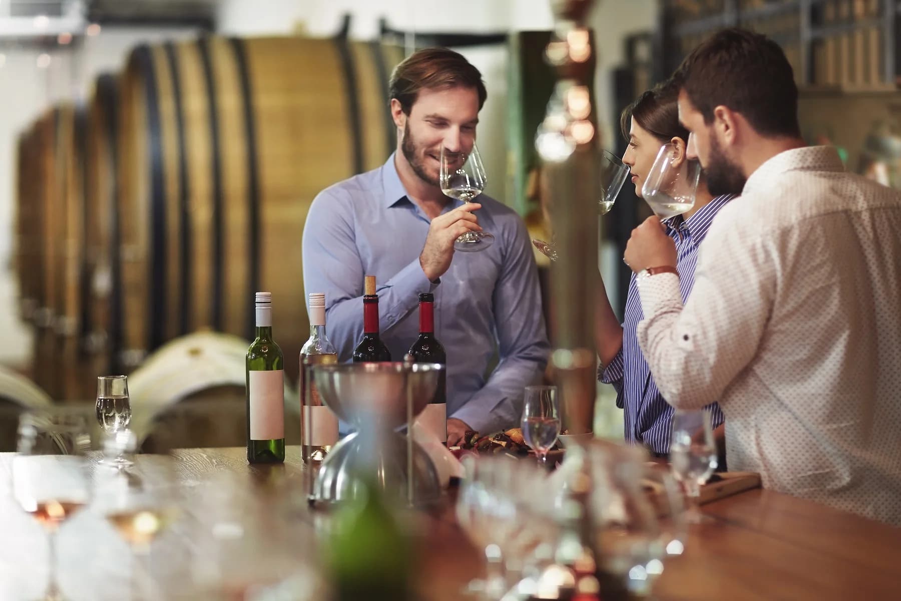 A group of three people enjoy wine tasting at a wooden bar in a winery.