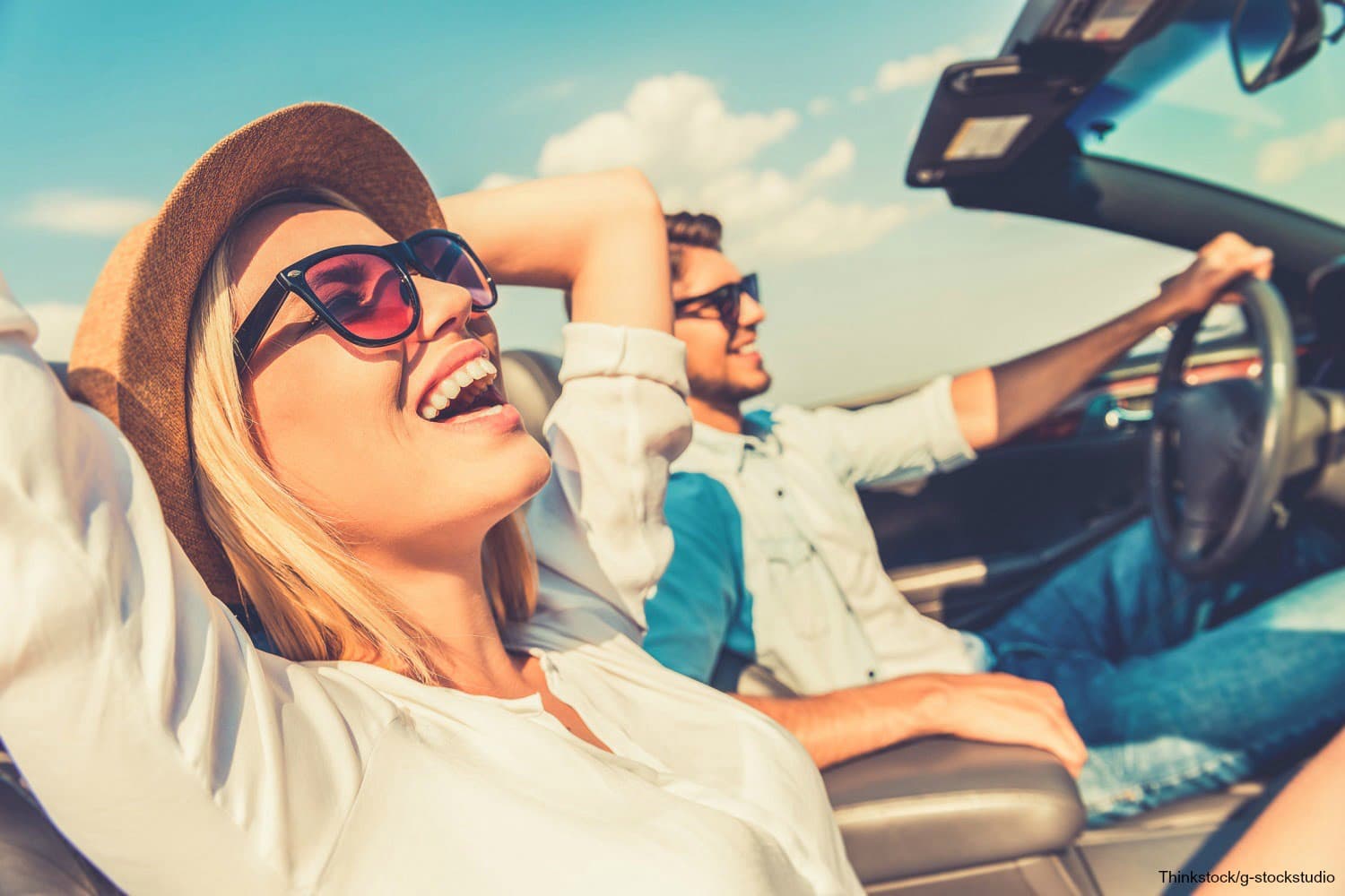 A smiling couple enjoys a road trip in a convertible under a sunny sky.