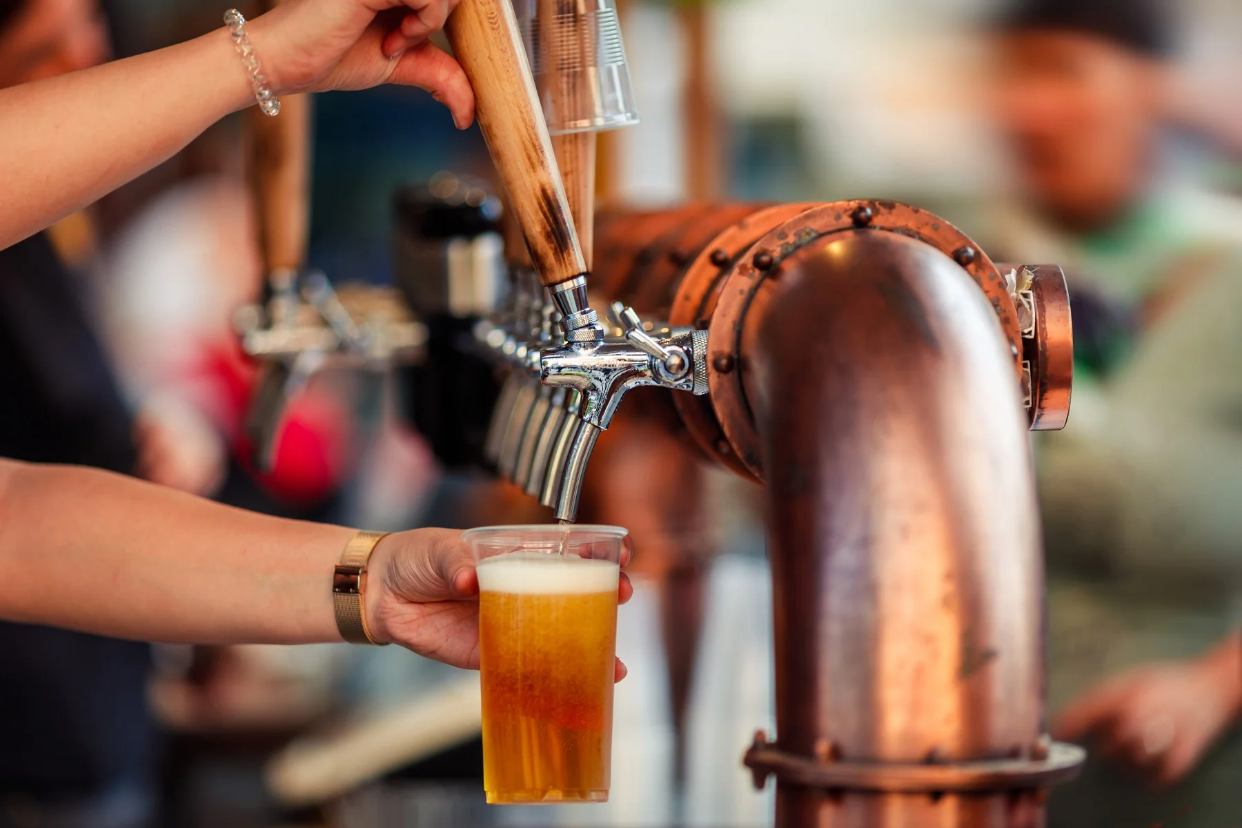 A person pours beer from a tap into a clear plastic cup.