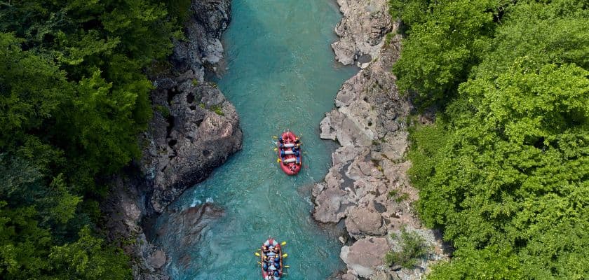 Aerial view of two colorful rafts navigating a serene, turquoise river surrounded by lush green foliage and rocky banks.