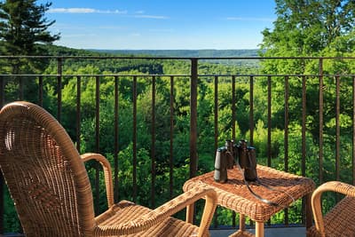A cozy balcony with a wicker chair and table overlooking a lush green landscape.