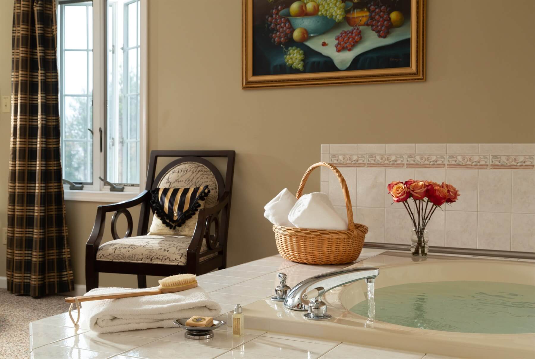 A cozy bathroom setting featuring a whirlpool tub, a wooden chair, and decorative elements like a basket and flowers.