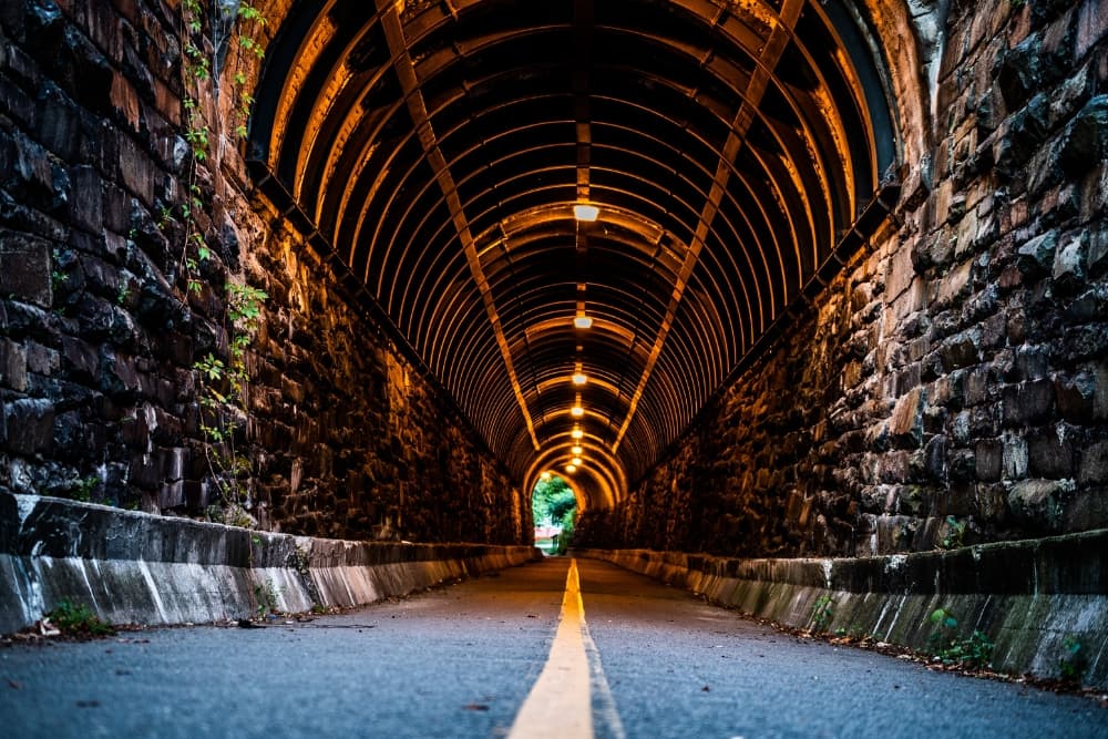 A tunnel with a stone archway and a road with a yellow line down the middle.