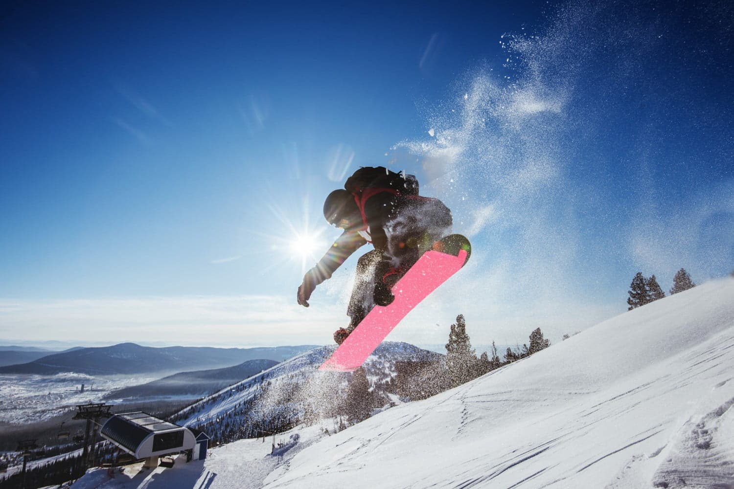 A snowboarder jumps while kicking up snow against a clear blue sky.