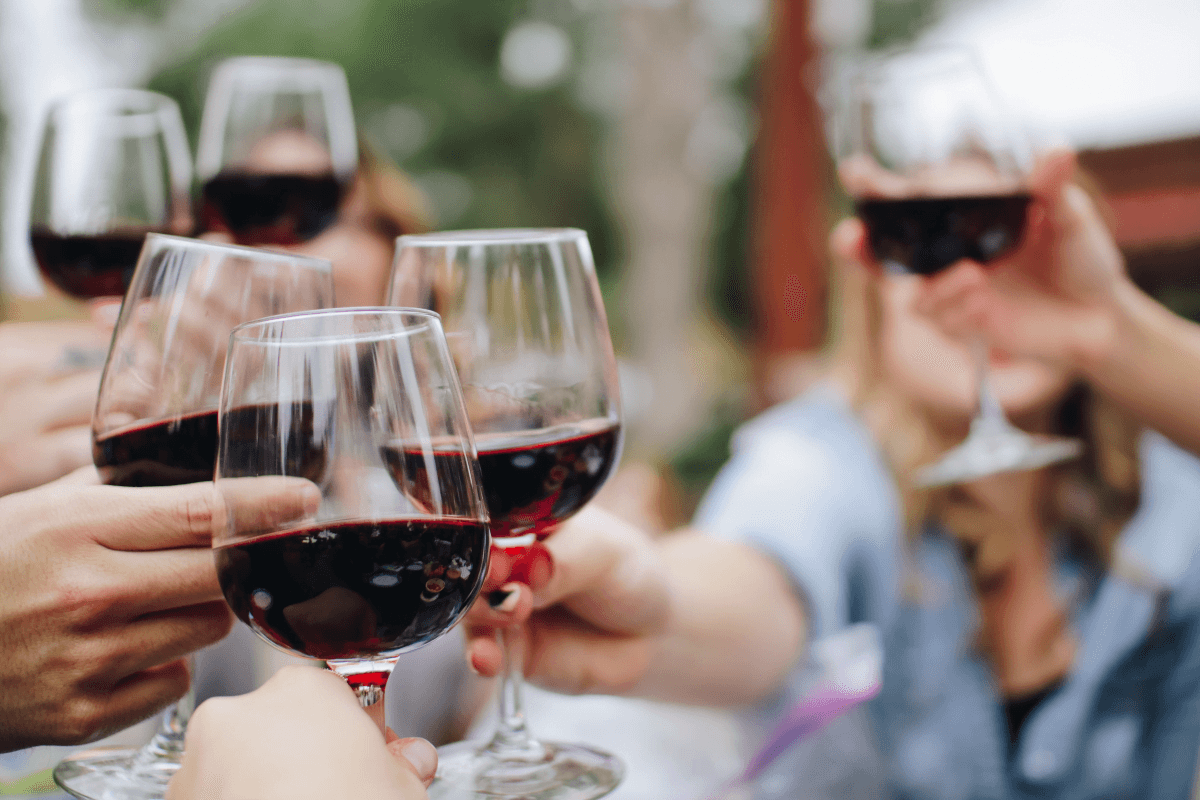 A group of people toasting with glasses of red wine outdoors. A group of people toasting with glasses of red wine outdoors.