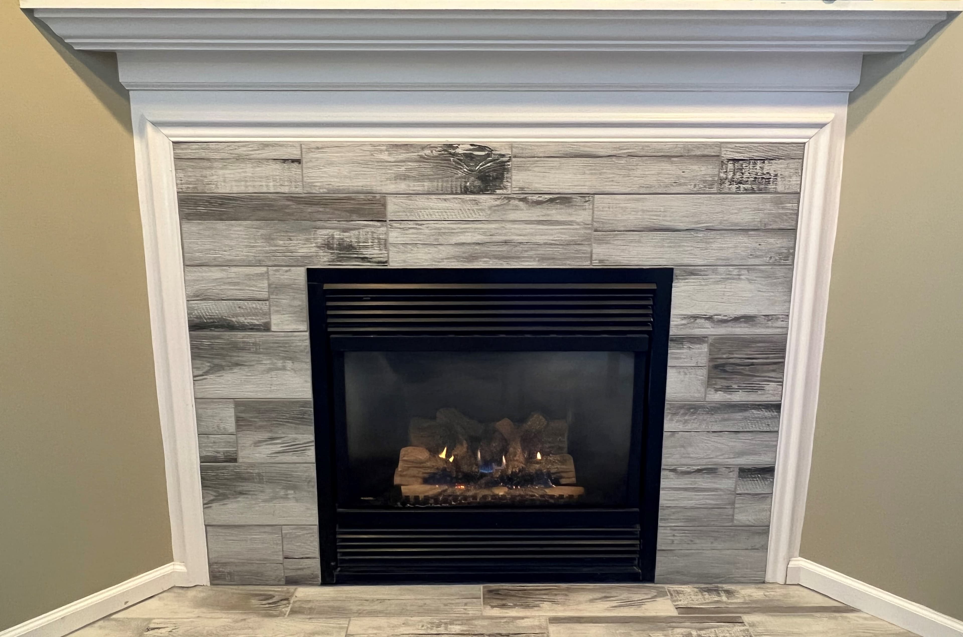 A modern fireplace with a black frame and gray wood-paneled wall.