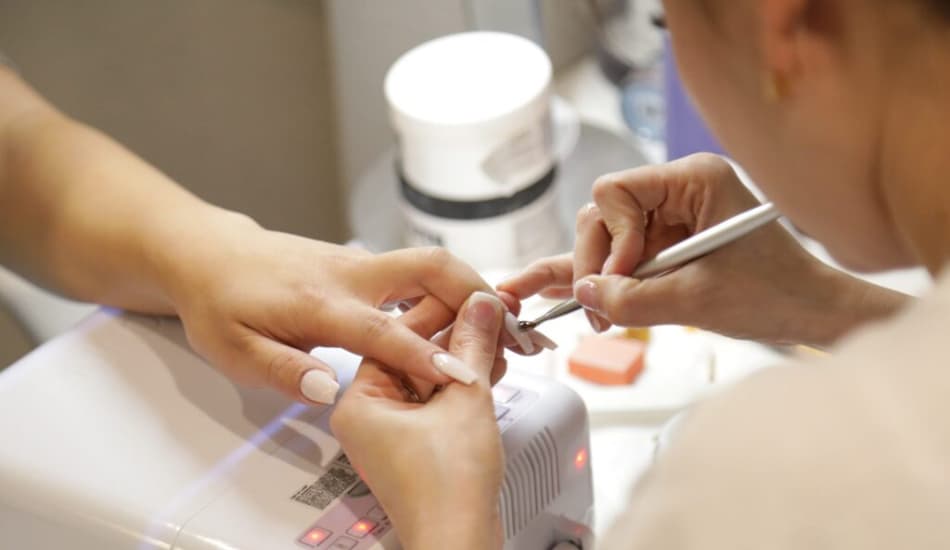 A woman getting her nails painted by a nail tech in a salon