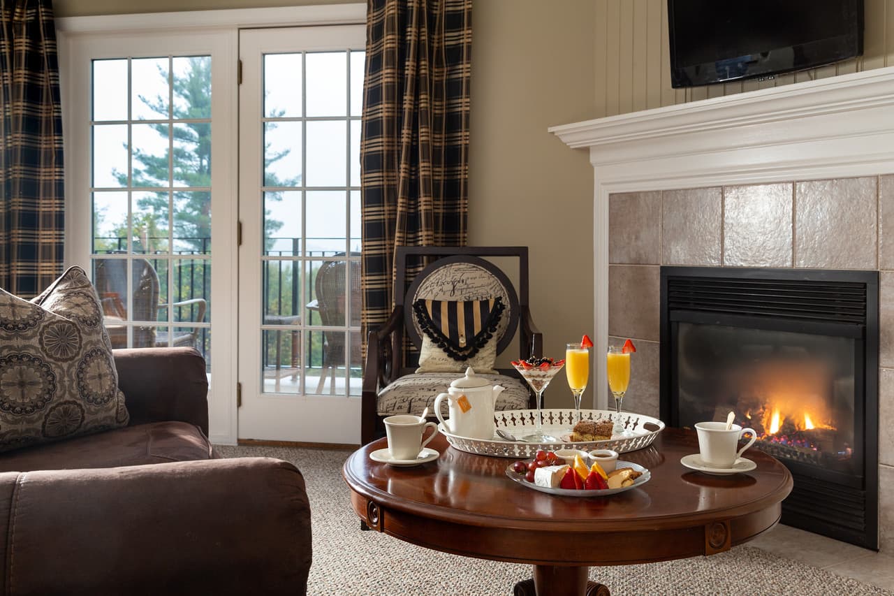 A cozy living area featuring a table with breakfast treats and drinks, near a fireplace and windows with a view.