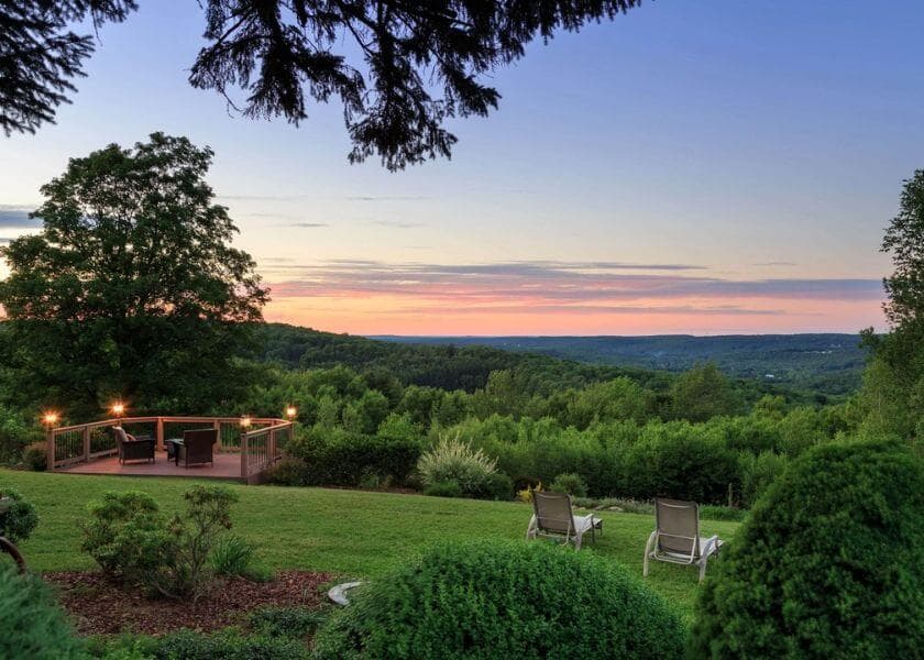 A serene landscape featuring lush greenery, a wooden deck, and two lounge chairs under a colorful sunset sky. A serene landscape featuring lush greenery, a wooden deck, and two lounge chairs under a colorful sunset sky.