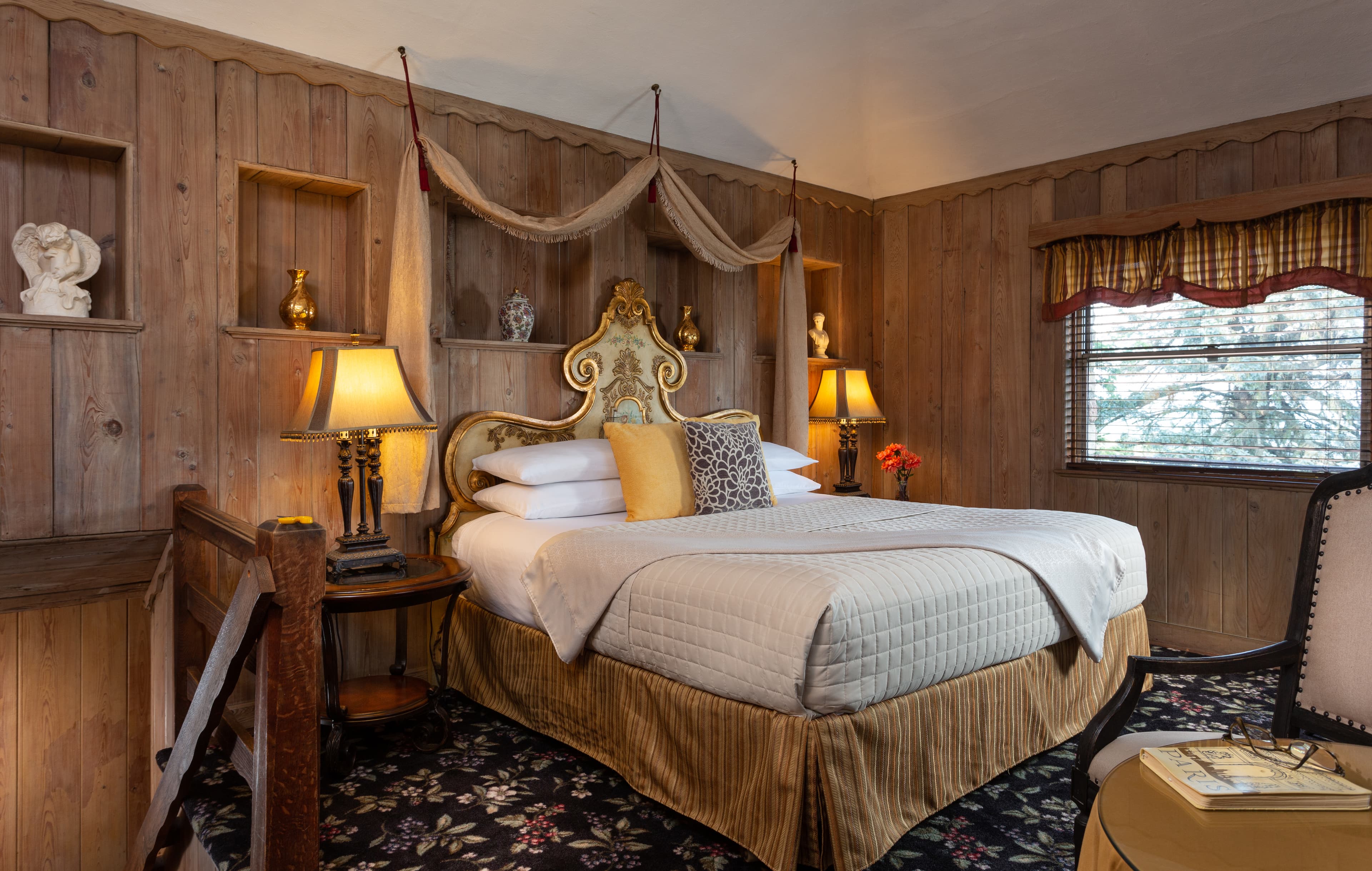A cozy bedroom featuring a large bed with decorative pillows, wooden walls, and warm lighting.