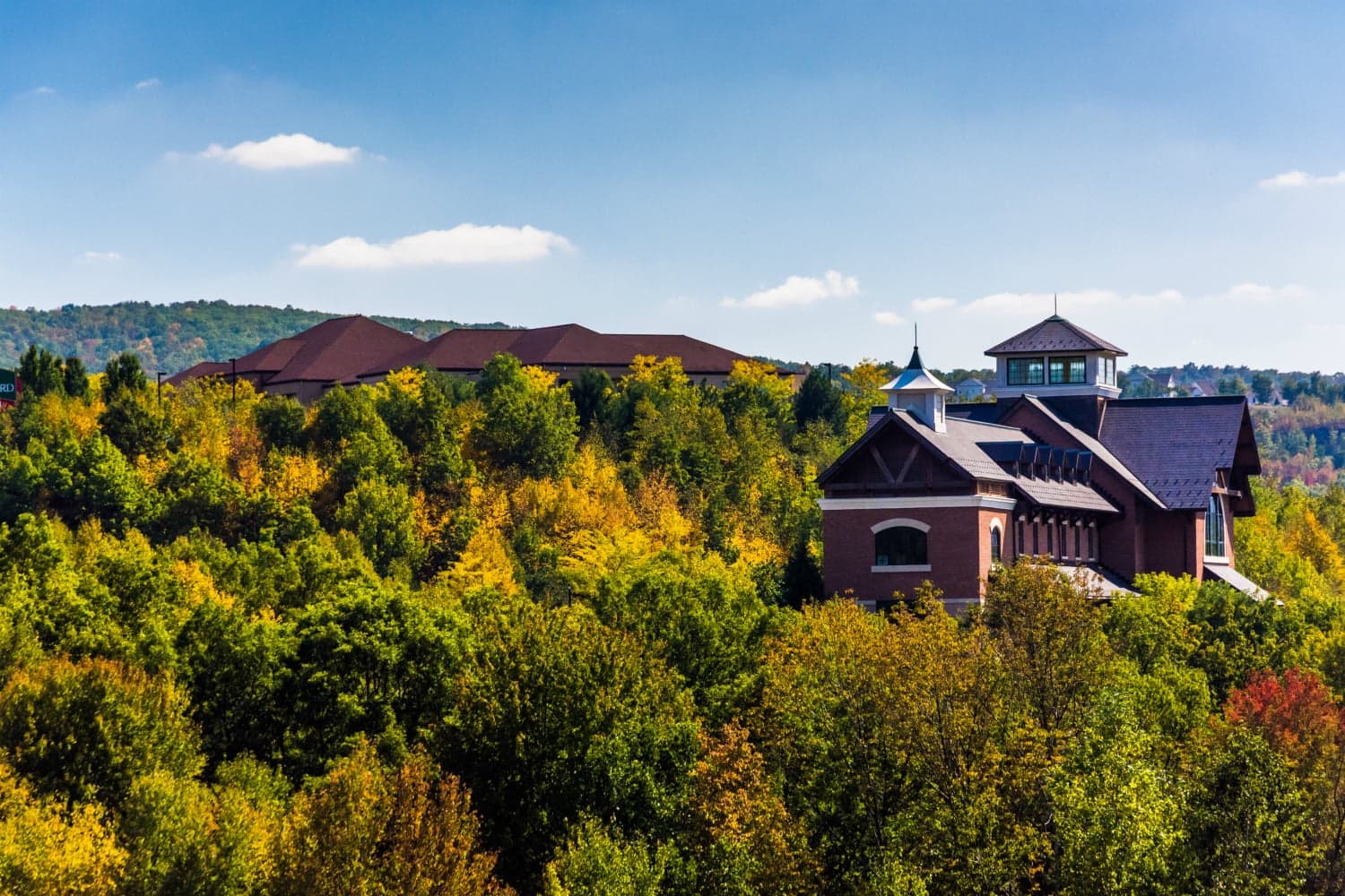 A scenic view of a building surrounded by vibrant autumn foliage and rolling hills under a clear blue sky.
