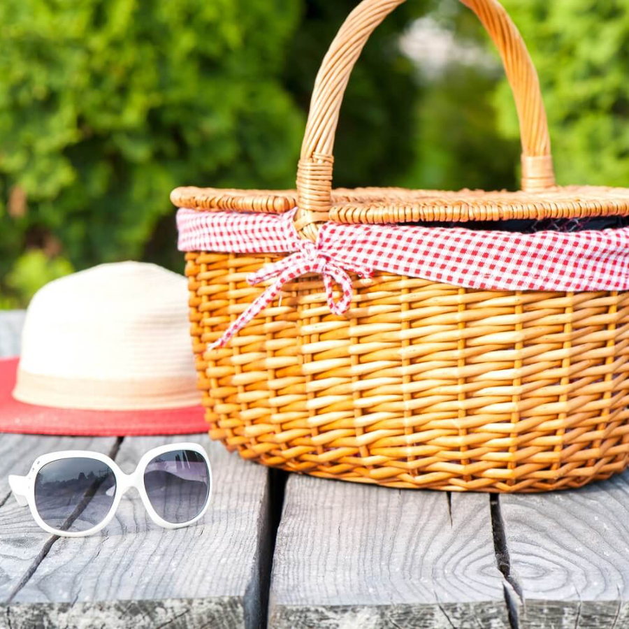 Picnic basket with white sun glasses and sun hat on wood picnic table