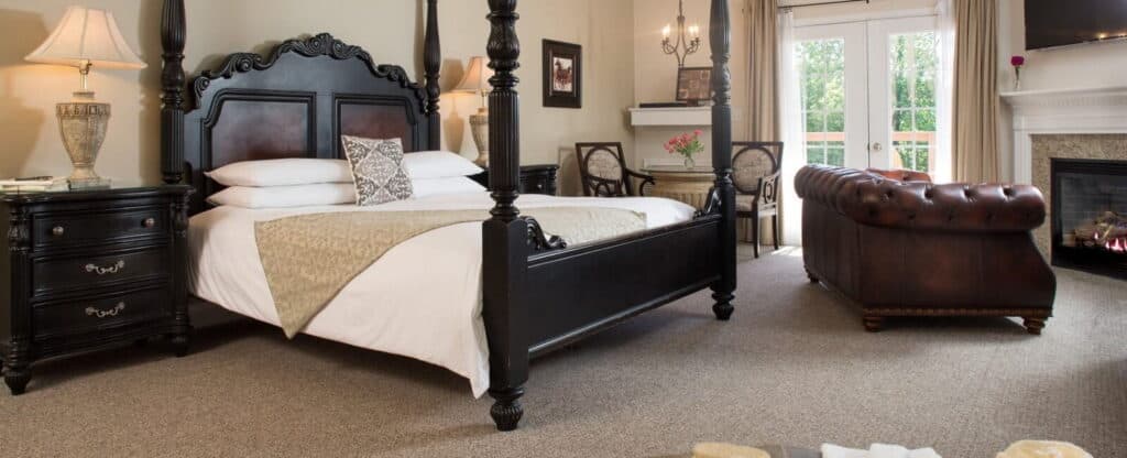 Luxurious hotel room featuring a four-poster bed, a leather couch, and natural light from large windows.