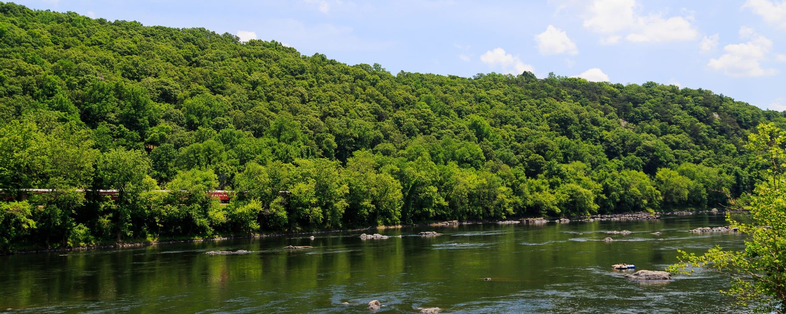 A tranquil river flows beside a lush, green hillside under a blue sky. A tranquil river flows beside a lush, green hillside under a blue sky.