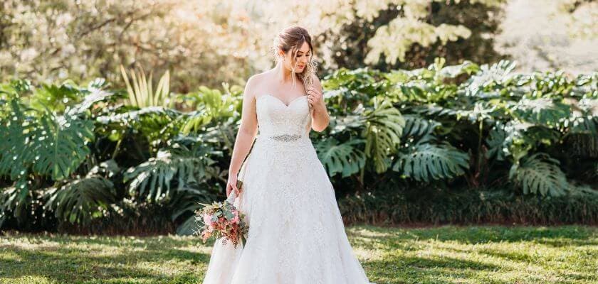 bride in lace wedding dress holding bouquet standing on grass in garden setting