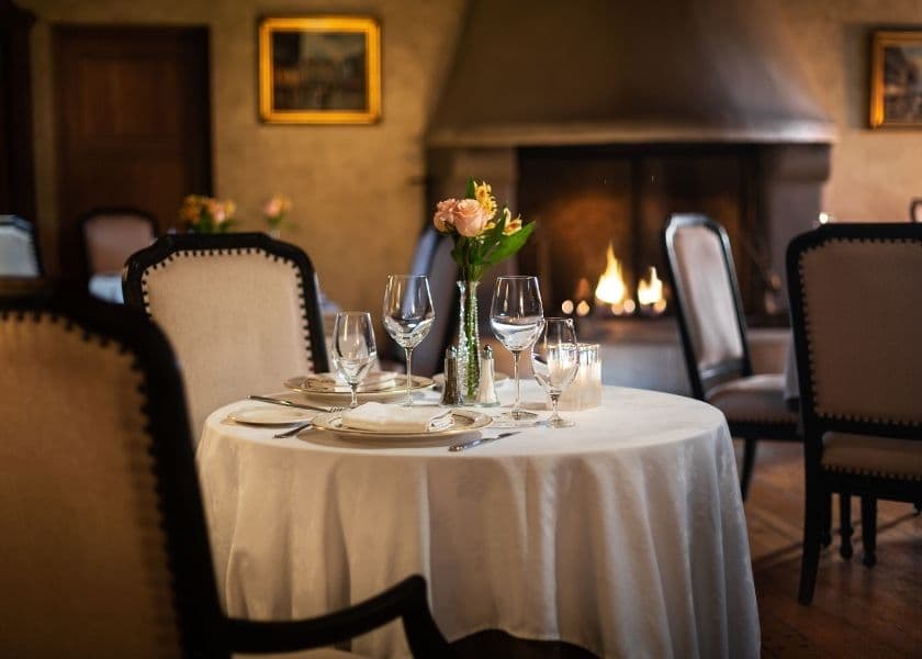 elegant set dining table with flowers and wine glasses in a cozy restaurant at the french manor with a lit fireplace in the background elegant set dining table with flowers and wine glasses in a cozy restaurant at the french manor with a lit fireplace in the background