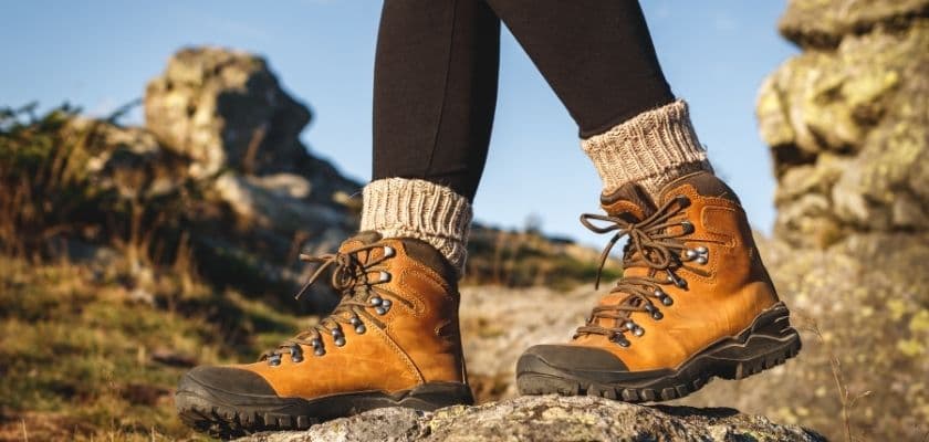 Hiking boots on rocky mountain terrain with warm sunlight, wool socks, and rugged stone in the background.