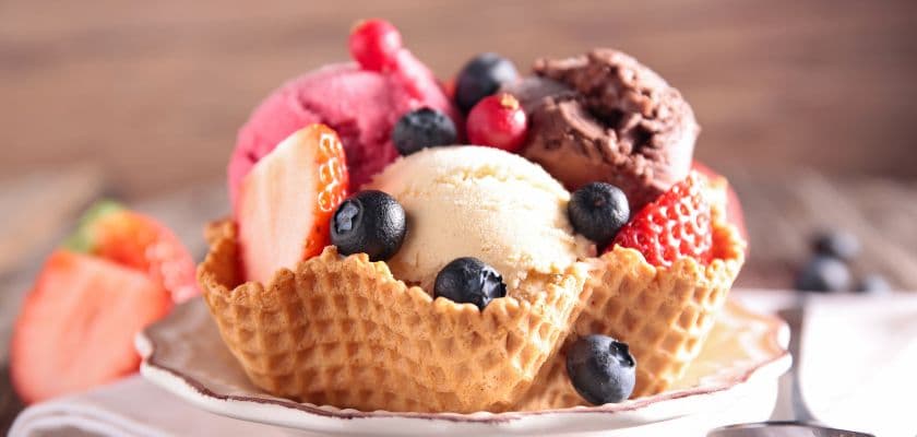 a waffle bowl filled with scoops of strawberry, vanilla, and chocolate ice cream, topped with blueberries and strawberries