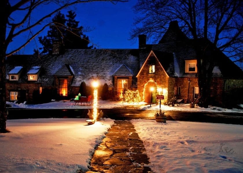 snow-covered stone inn at night with warm lights glowing and holiday decorations by the entrance snow-covered stone inn at night with warm lights glowing and holiday decorations by the entrance