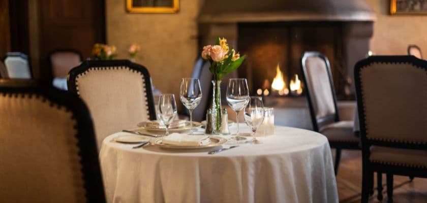 elegant restaurant table set for dinner with wine glasses and flowers near cozy fireplace