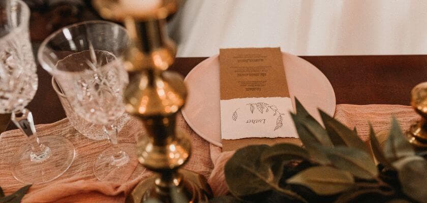 wedding table setting with crystal glasses menu on plate gold candle holder and greenery decoration